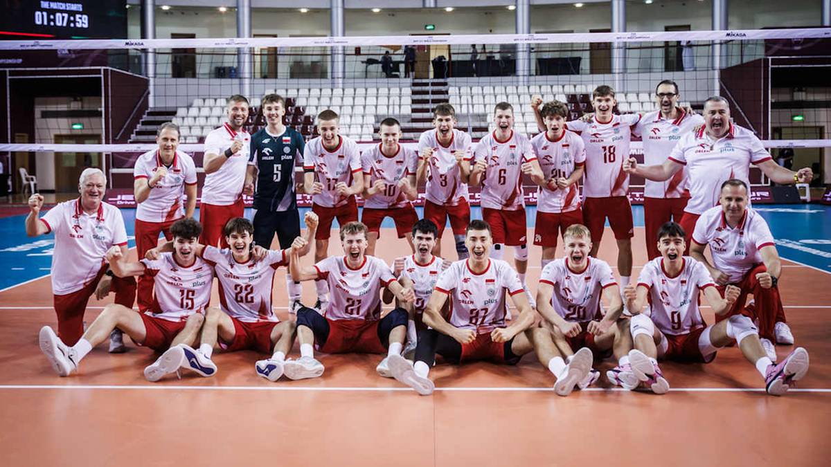 Drużyna siatkarzy w białych i czerwonych strojach pozuje do zdjęcia na boisku siatkarskim.