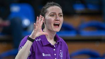 Kobieta w fioletowej koszulce z kr&oacute;tkim rękawem, z otwartymi ustami i gestykulującą prawą dłonią, patrząca w kierunku widza.