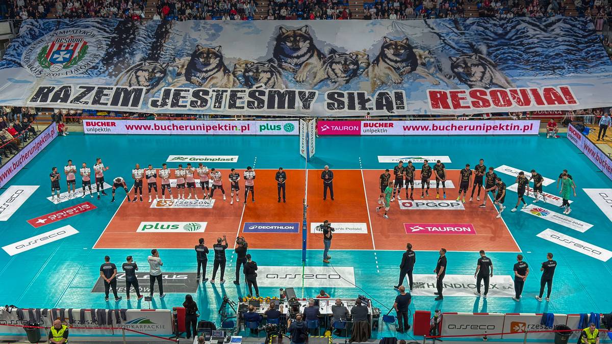 Widok z g&oacute;ry na boisko do siatk&oacute;wki podczas meczu PlusLigi, z zawodnikami na parkiecie i kibicami na trybunach.