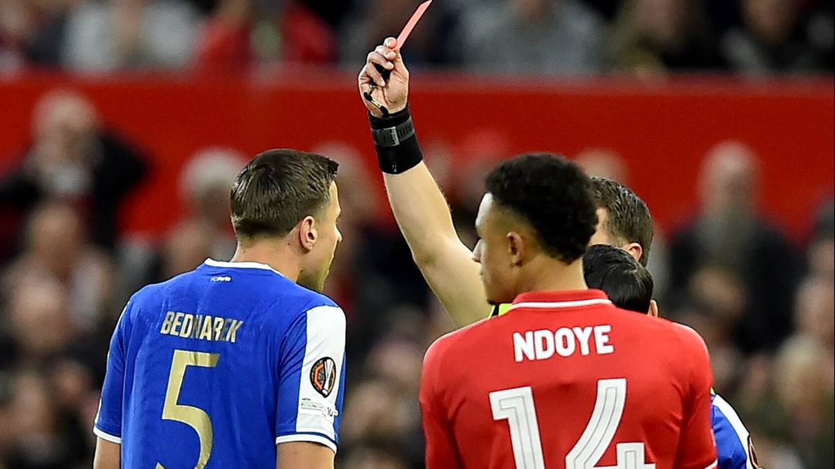 Sędzia pokazuje czerwoną kartkę zawodnikowi w czerwonej koszulce.