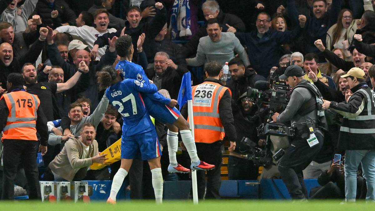 Dwóch piłkarzy w niebieskich strojach świętuje zdobycie gola na boisku. Wokół nich znajduje się tłum kibiców i ekipa telewizyjna.