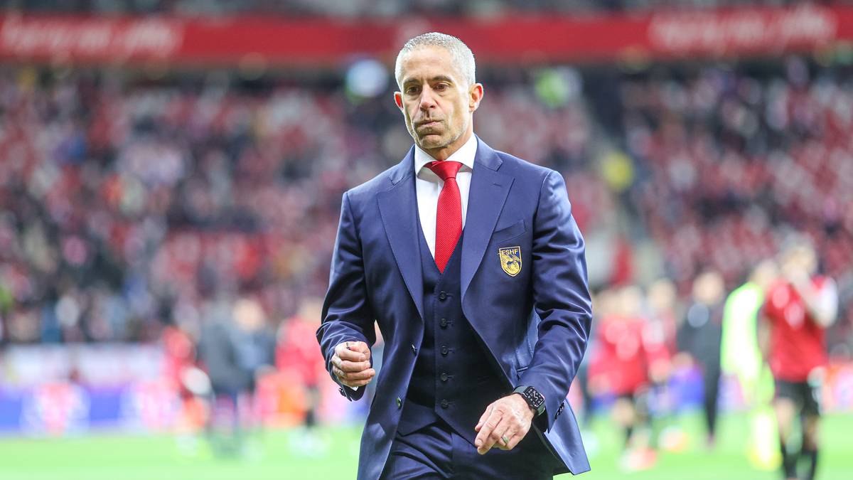 Sylvinho, trener reprezentacji Albanii, w garniturze na boisku piłkarskim.