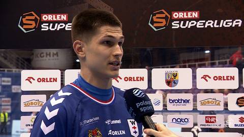 Młody mężczyzna w niebieskiej koszulce sportowej udziela wywiadu do mikrofonu na tle tablic z logo "ORLEN SUPERLIGA".