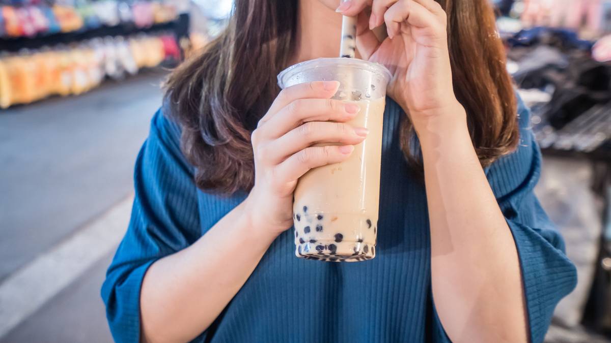 Kobieta trzyma kubek z bubble tea, popijając przez słomkę.