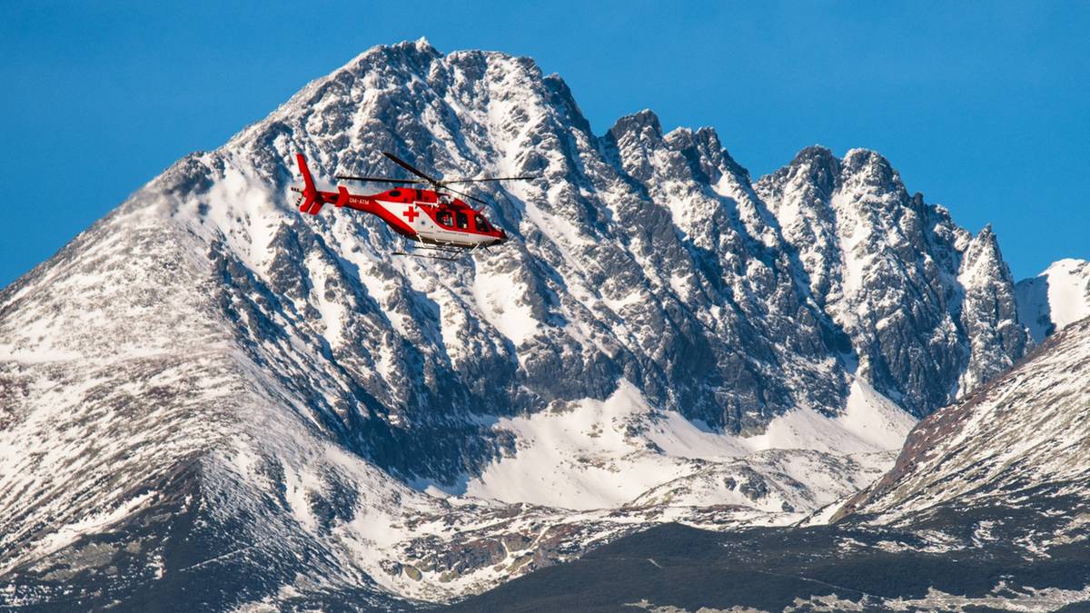 Czerwono-biały helikopter ratowniczy latający na tle ośnieżonych g&oacute;r.