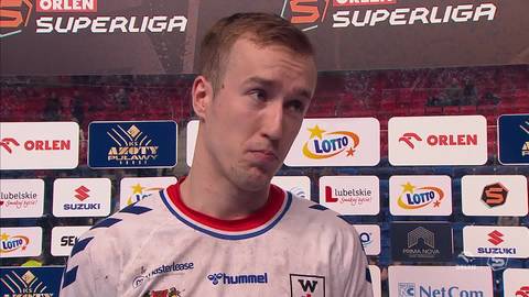 Portret Jakuba Będzikowskiego, zawodnika siatk&oacute;wki, w białej koszulce z czerwonymi i niebieskimi elementami. Na jego twarzy widać zmęczenie i skupienie.