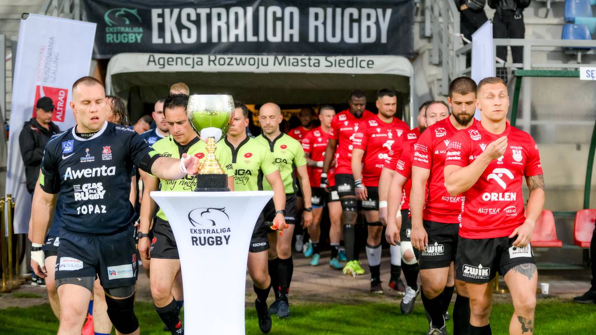 Zawodnicy drużyn rugby wychodzący z tunelu na boisko, z pucharem na pierwszym planie.
