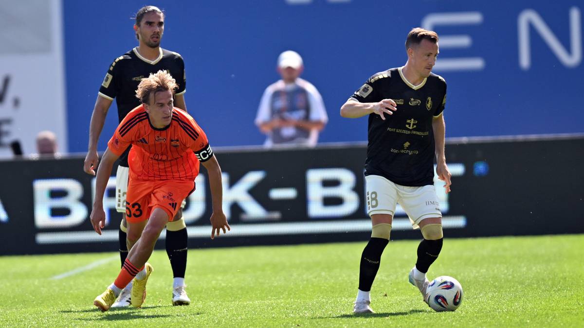 Dwóch piłkarzy w koszulkach drużyny w kolorze czarnym z żółtymi elementami oraz jeden piłkarz w pomarańczowej koszulce z numerem 33, grających w piłkę nożną na zielonym boisku.