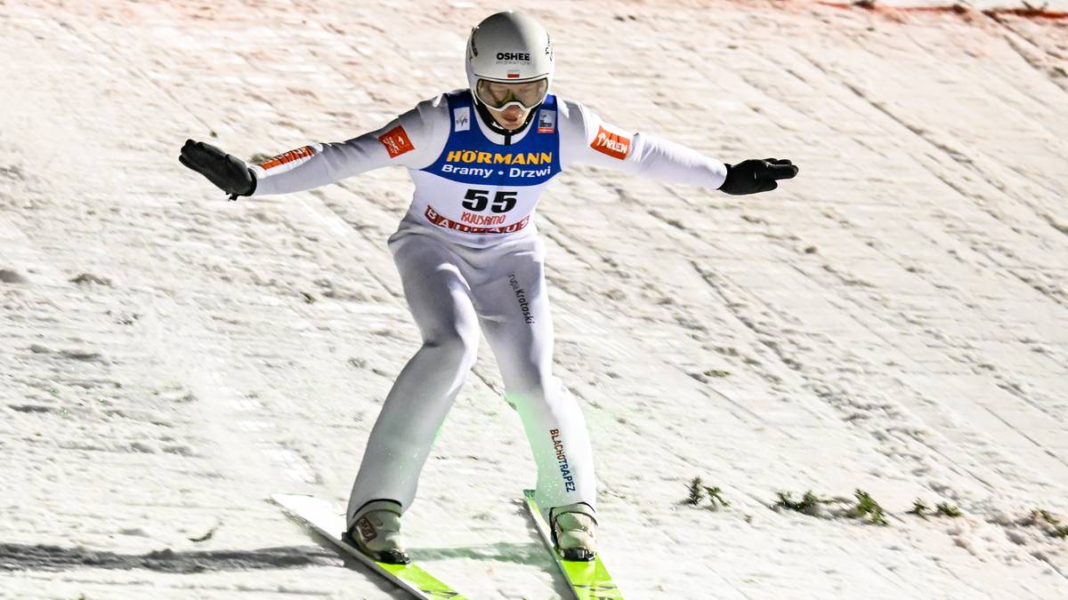 Skoczek narciarski w białym kombinezonie z numerem 55 na rozbiegu.