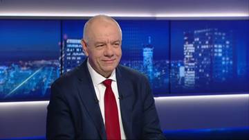 Mężczyzna w garniturze i krawacie siedzi na tle nocnej panoramy miasta.