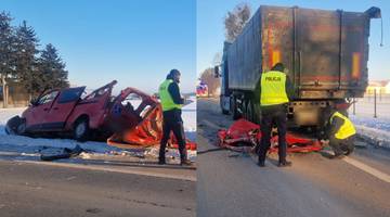 Rozbity czerwony bus po wypadku drogowym, obok widoczny fragment ciężar&oacute;wki i policjanci.