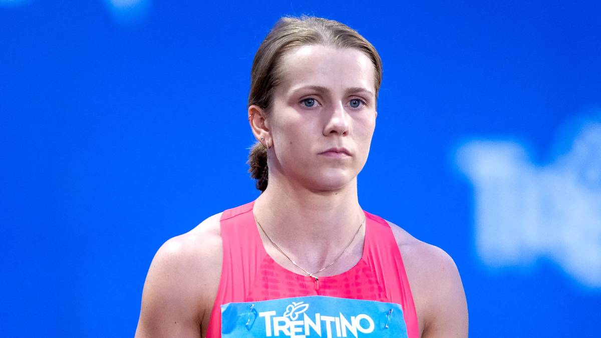 Portret lekkoatletki w okularach sportowych i różowym stroju, z zapiętym niebieskim tabliczką z napisem "TRENTINO" na piersi. Patrzy wprost przed siebie z poważną miną.