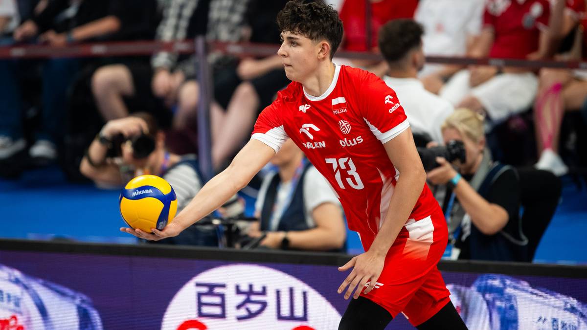 Młody siatkarz w czerwonym stroju reprezentacji Polski, z numerem 73, trzymający piłkę do siatkówki w lewej ręce.