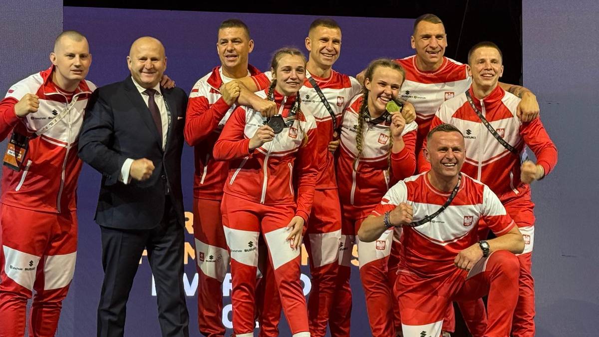 Grupa polskich medalist&oacute;w bokserskich w strojach sportowych i jeden mężczyzna w garniturze pozuje do zdjęcia z medalami.