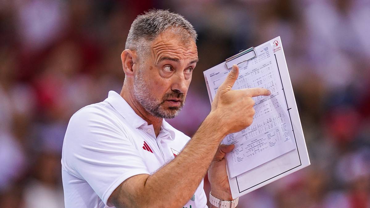 Mężczyzna w białej koszulce z krótkim rękawem trzyma kartkę z zapiskami i wskazuje na nią palcem.