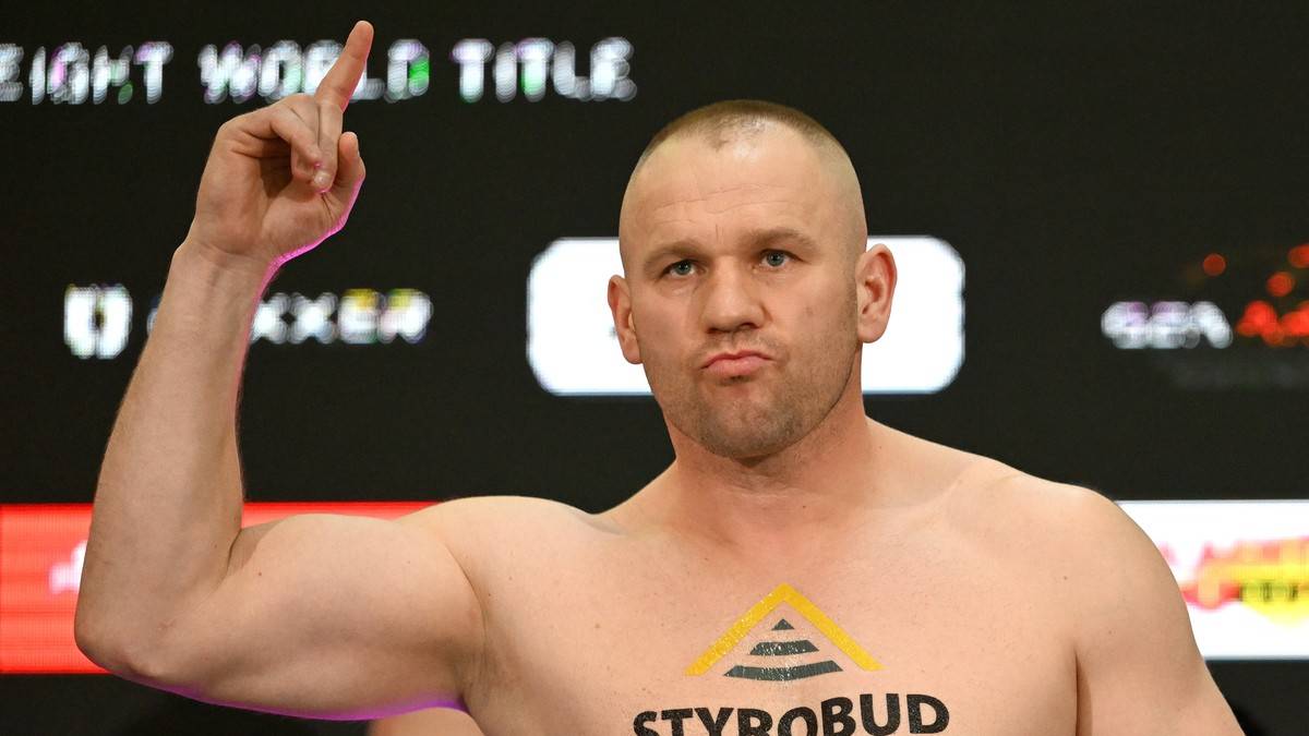 Mężczyzna z uniesioną ręką, prawdopodobnie bokser, z logo na klatce piersiowej.