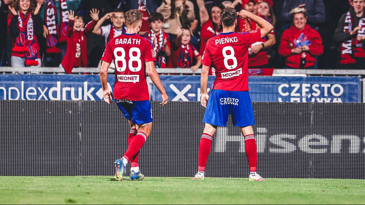 Dwóch piłkarzy w czerwonych koszulkach i niebieskich spodenkach stoi na boisku piłkarskim, plecami do widza. Jeden z nich ma na koszulce numer 88, drugi numer 8. W tle widać kibiców na trybunach.