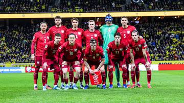 Drużyna piłkarska w czerwonych strojach na tle stadionu.