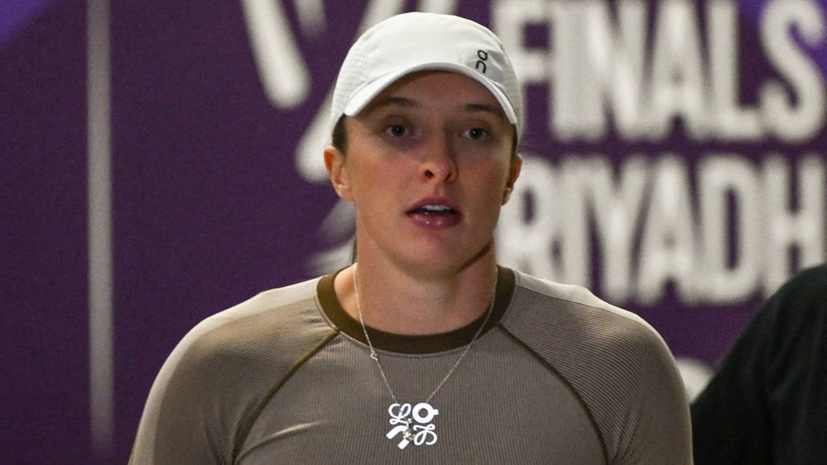 Iga Świątek w stroju sportowym, stojąca na tle fioletowej ściany z logo WTA Finals Riyadh.