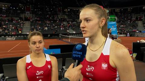 Dwie zawodniczki tenisa w czerwonych strojach sportowych, jedna z nich udziela wywiadu do mikrofonu Polsat Sport.