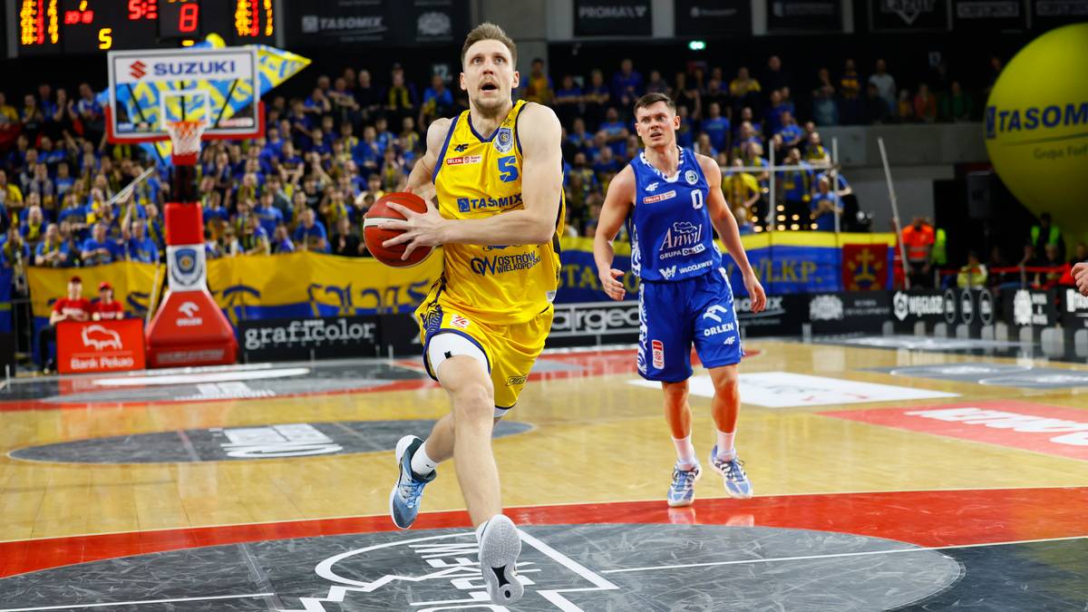 Koszykarz w żółtej koszulce z numerem 9 prowadzi piłkę, drugi zawodnik w niebieskiej koszulce biegnie za nim.