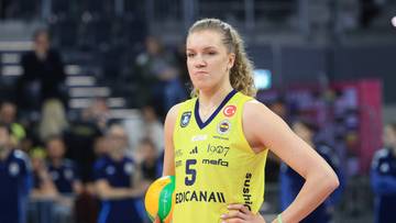 Siatkarka w ż&oacute;łtej koszulce z numerem 5 trzyma piłkę do siatk&oacute;wki.