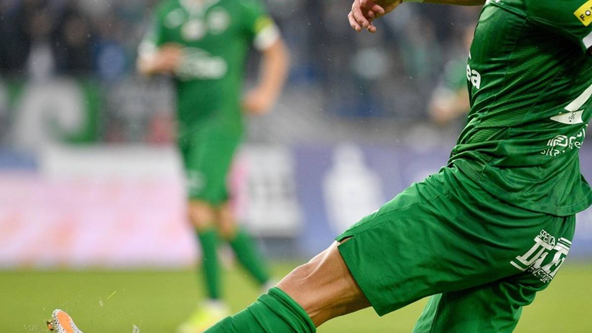 Piłkarz w zielonym stroju kopie piłkę na boisku.