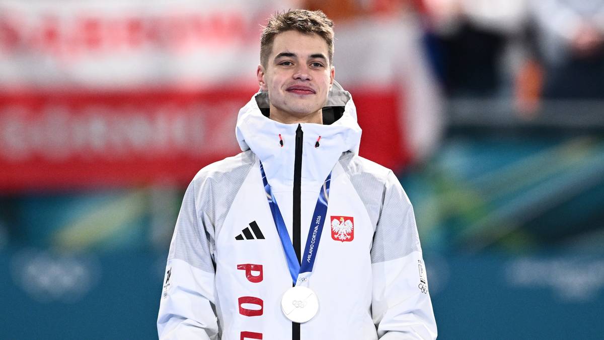 Władimir Semirunnij na podium z medalem olimpijskim, ubrany w białą kurtkę z polskimi barwami.