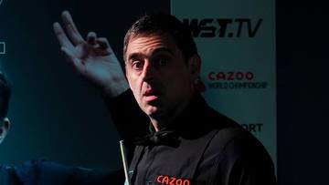 Ronnie O'Sullivan, znany snookerzysta, wskazuje palcem na bok, ubrany w czarną koszulę z muszką.
