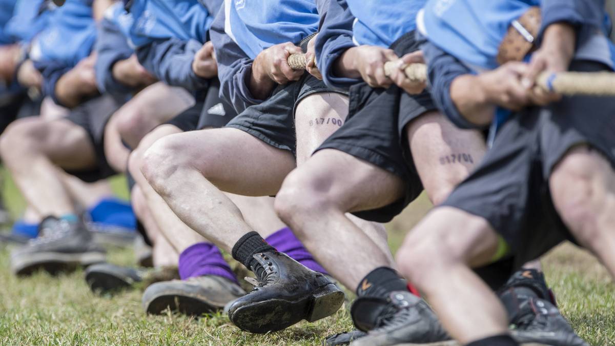 Drużyna w niebieskich koszulkach i czarnych spodenkach walczy w przeciąganiu liny.