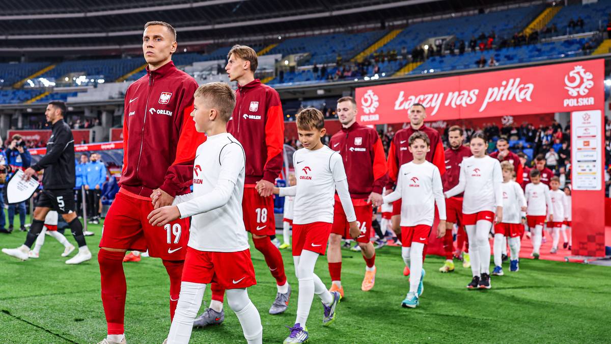 Piłkarze reprezentacji Polski w czerwonych strojach wraz z dziećmi wychodzą na murawę stadionu.