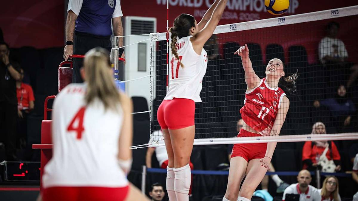 Siatkarka w białej koszulce z numerem 17 wykonuje wysoki atak nad siatką, podczas gdy inna zawodniczka w czerwonej koszulce z numerem 11 stara się ją zablokować.