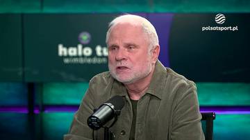 Starszy mężczyzna z siwą brodą i włosami siedzi przed mikrofonem w studiu telewizyjnym. Za nim widnieje ekran z napisem "halo tu wimbledon".