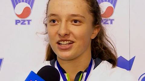 Zbliżenie na twarz Igi Świątek, polskiej tenisistki, podczas wywiadu po zawodach. Ma na sobie medal i słuchawki na szyi.