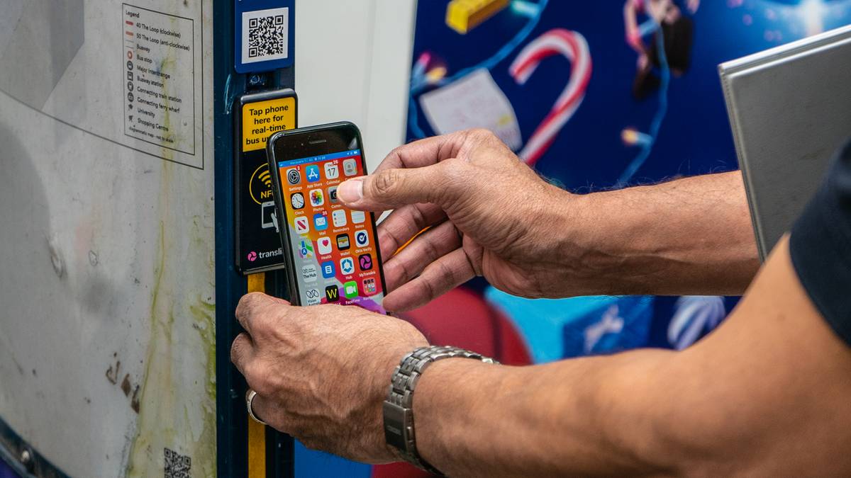 Osoba skanuje smartfonem kod QR na przystanku autobusowym, obok stoi osoba z białą laską.