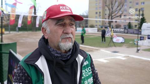 Janusz Danek w czerwonej czapce z daszkiem i kamizelce, na tle toru żużlowego.