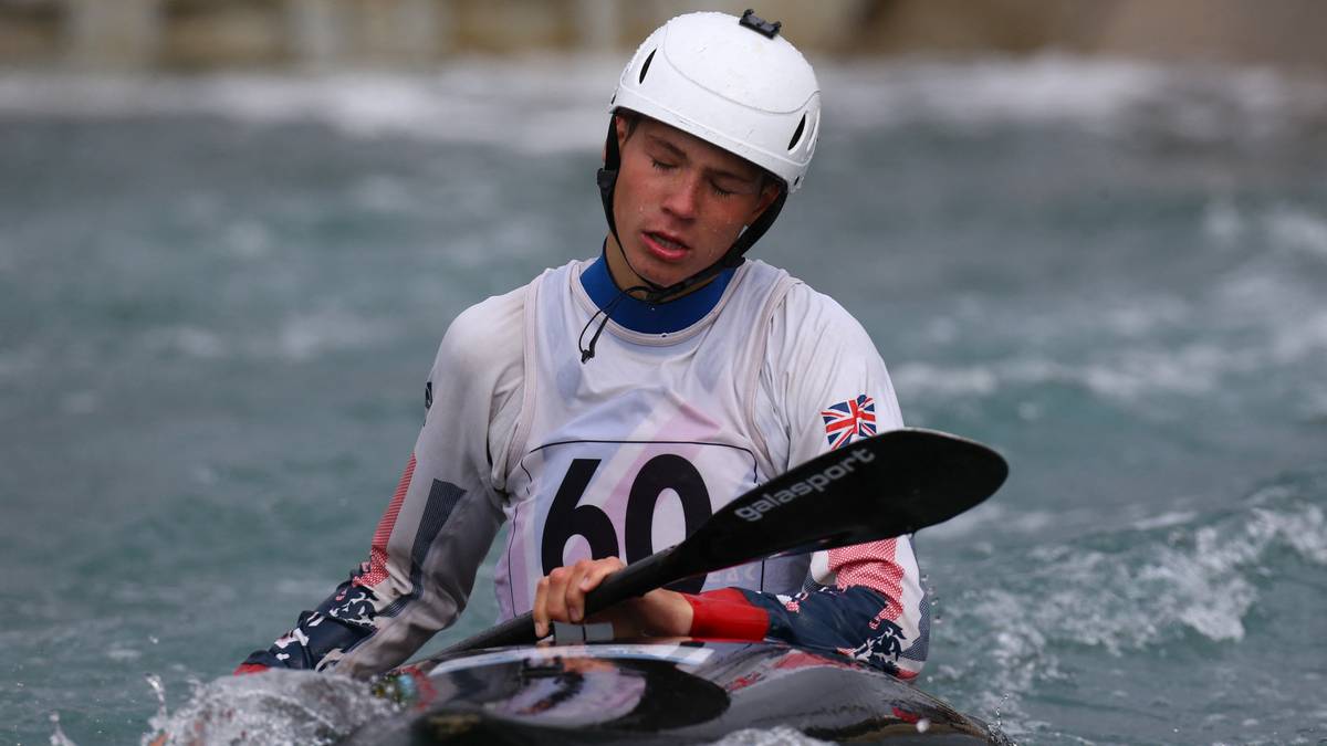 Mężczyzna w białym kasku i stroju sportowym z numerem 60 na piersi siedzi w kajaku.