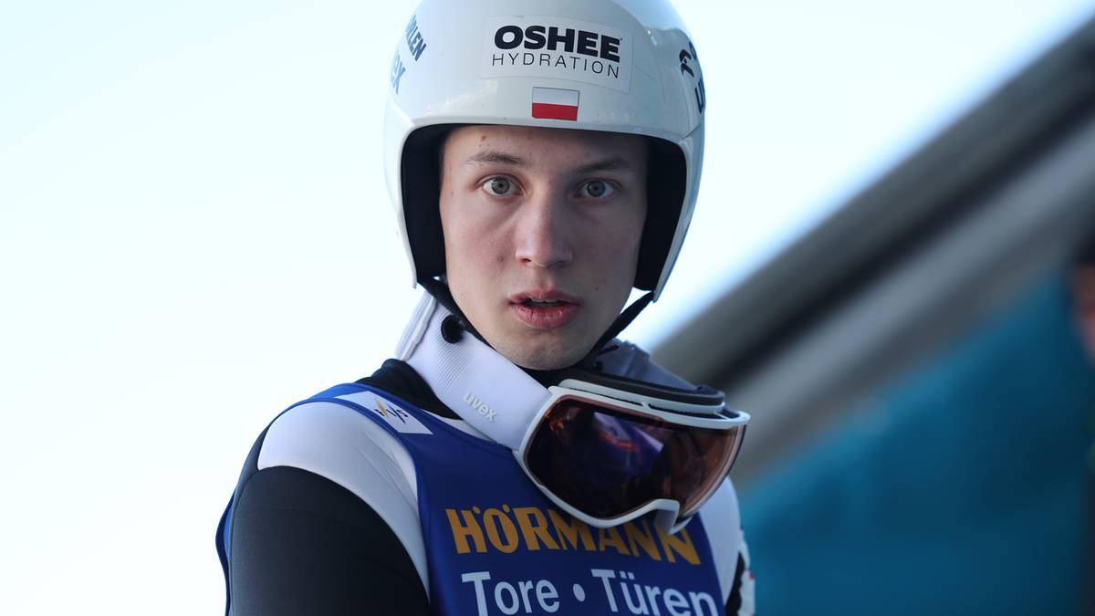 Młody mężczyzna w białym kasku z napisami "OSHEE HYDRATION" i niebiesko-białym stroju sportowym z logo "Hormann" i numerem "58", noszący gogle narciarskie.