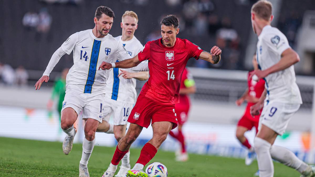 Piłkarze w białych strojach reprezentacji Finlandii i czerwonych strojach reprezentacji Polski rywalizują o piłkę na boisku piłkarskim podczas meczu.