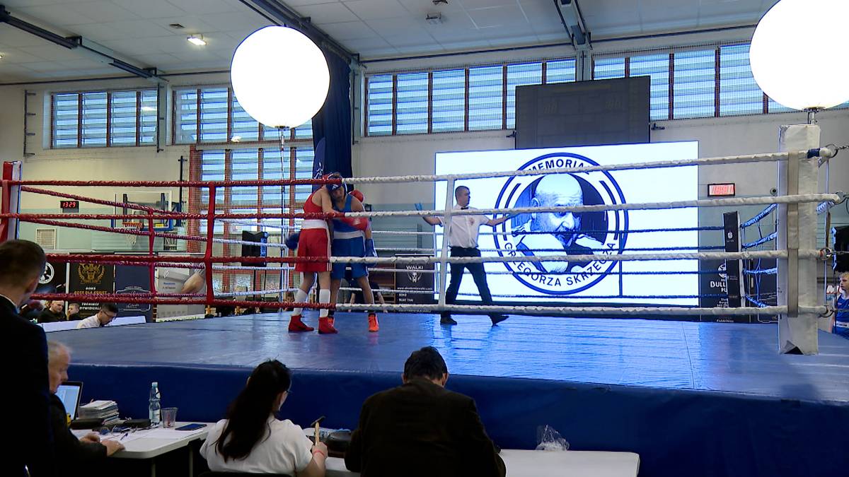 Ring bokserski podczas IV Memoriału Grzegorza Skrzecza z dwoma zawodnikami i sędzią na ringu, a w tle ekran z logo memoriału.