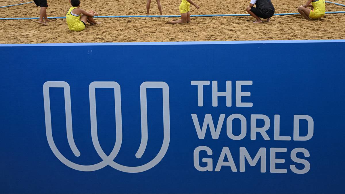 Logo The World Games na niebieskim tle, z widocznymi fragmentami boiska do siatkówki plażowej i grających zawodników w tle.