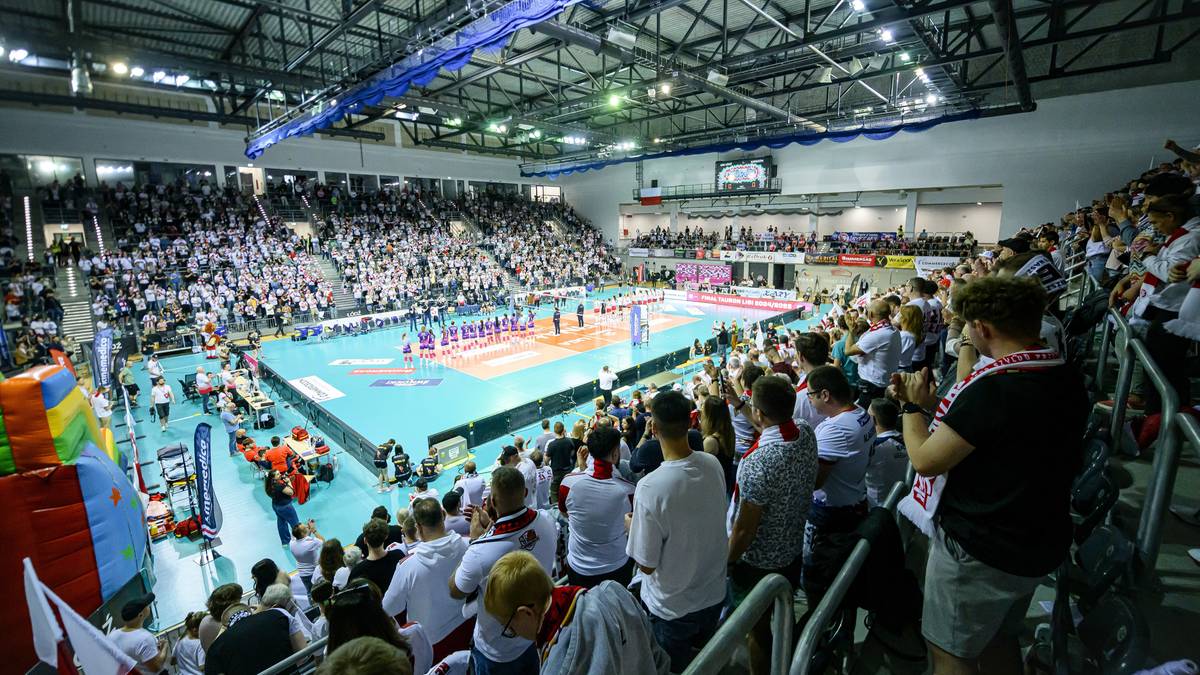 Widownia wypełniona po brzegi kibicami obserwuje mecz siatkówki rozgrywany na hali sportowej.