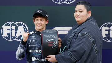Kierowca Formuły 1 Antonelli odbiera trofeum na podium w towarzystwie mężczyzny w stroju japońskim.