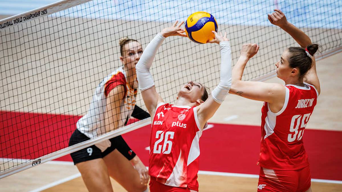 Trzy siatkarki w czerwonych strojach, dwie z nich próbują zatrzymać atak trzeciej zawodniczki z piłką nad głową.