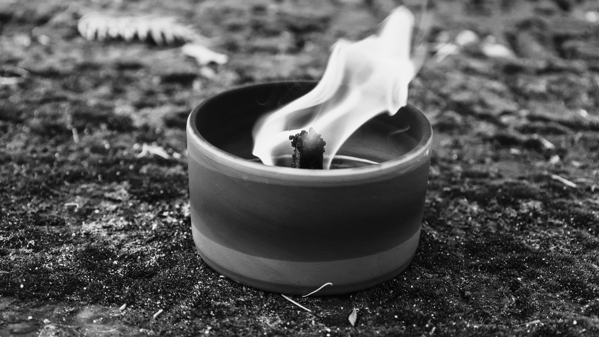 Mała, ceramiczna świeca z płomieniem na kamienistym podłożu.