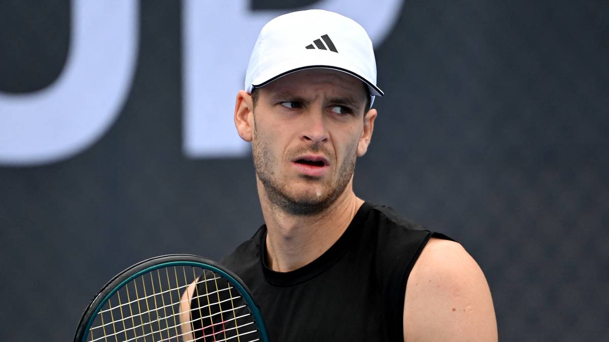 Tenisista w białej czapce i czarnym stroju z rakietą tenisową.