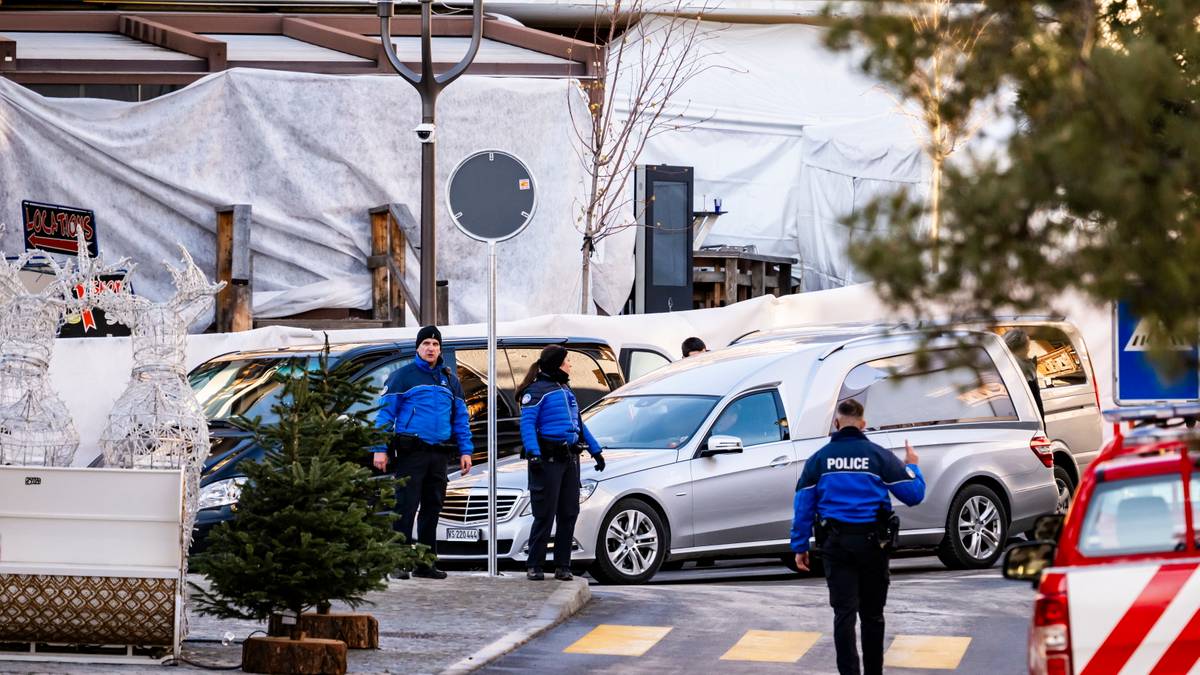 Policjanci w mundurach stoją obok karawanu pogrzebowego i radiowozu.