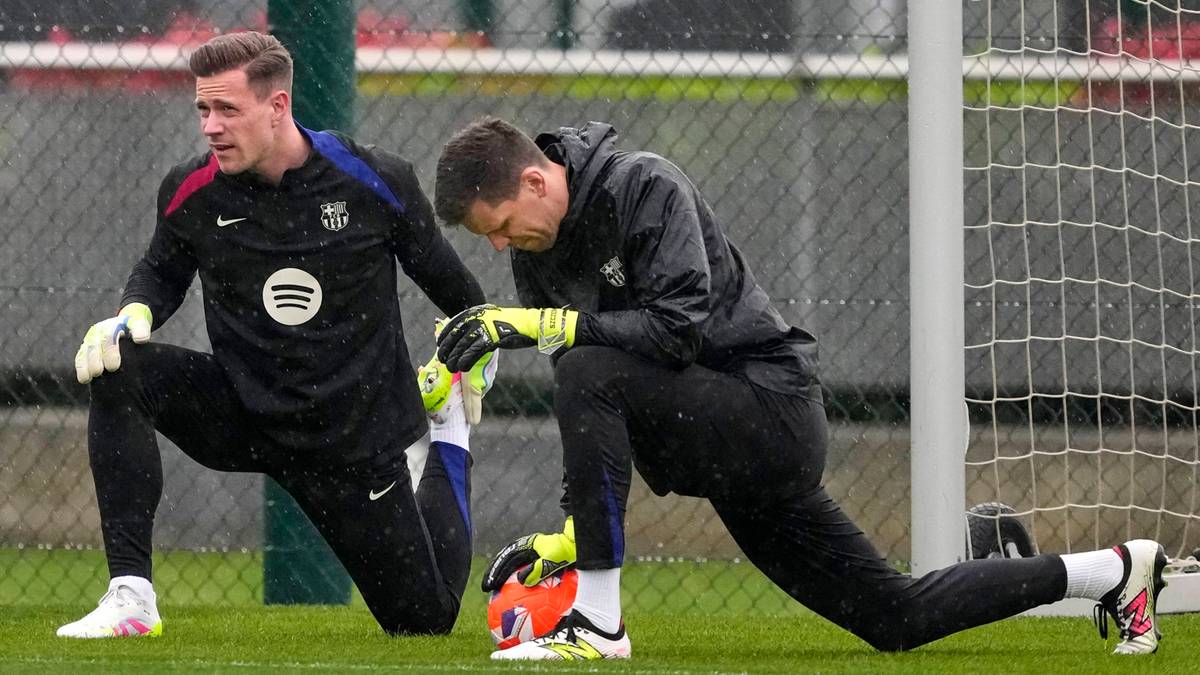 Dwóch piłkarzy grających na pozycji bramkarza, wykonujących ćwiczenia rozciągające na zielonej murawie.