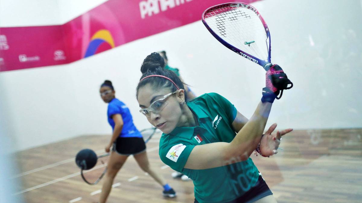 Zawodniczka w okularach i zielonej koszulce odbija piłkę do gry w squasha lub racquetball rakietą.