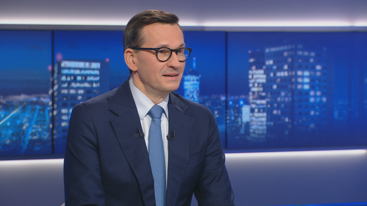 Mateusz Morawiecki w okularach i garniturze, siedzący w studiu telewizyjnym.
